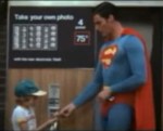 Superman gives his picture to the boy who just paid at the photo booth.